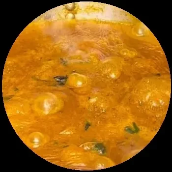 Close-up of bubbling, orange sauce with green specks.