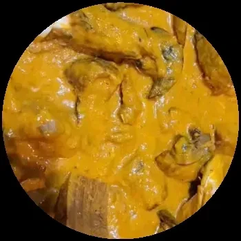 Circular close-up of food with pieces in thick orange-yellow sauce.
