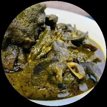 Close-up of a dark green stew with meat in a white bowl.