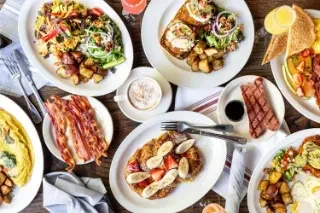 Overhead shot of a wooden table laden with various breakfast dishes.