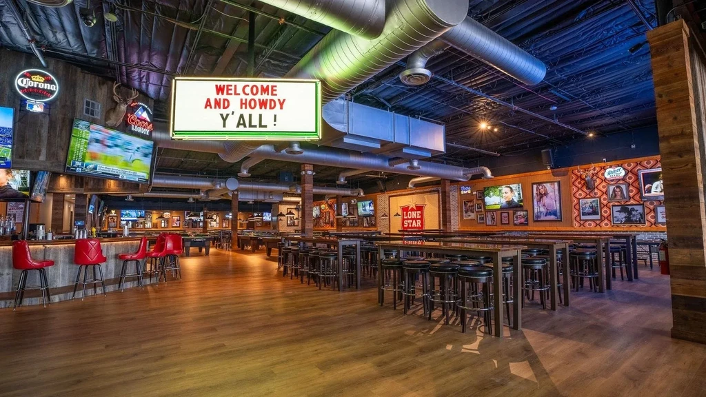 Dimly lit bar with multiple flat-screen TVs and a "Howdy Y'all!" sign.