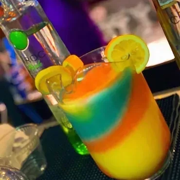 Multi-layered frozen drink with yellow, orange, and blue layers, garnished with citrus.