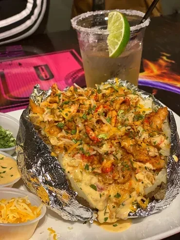 Baked potato with crawfish, cheese, sauce, herbs, and drink.