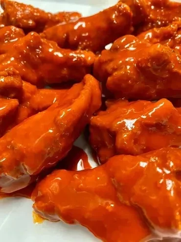 Close-up of boneless chicken pieces coated in a reddish-orange sauce.