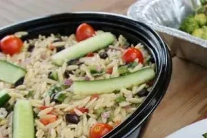 Orzo pasta salad with vegetables in a black take-out container.