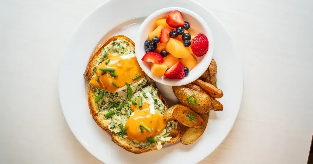 Breakfast plate with poached eggs, toast, fruit, and potato wedges.
