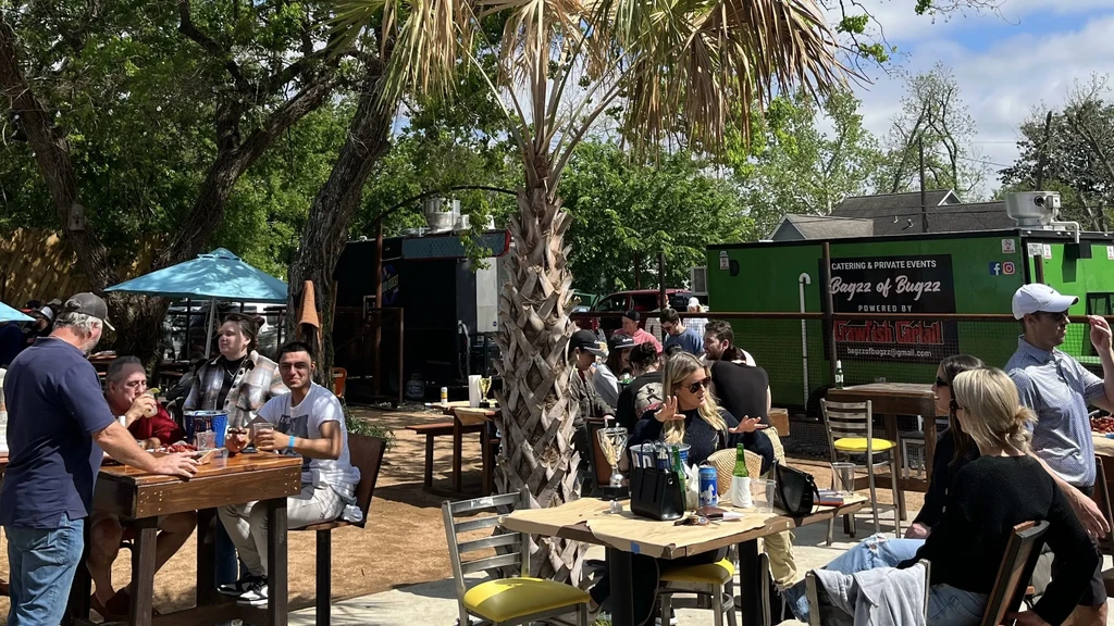 Outdoor restaurant patio with patrons, palm tree, and catering truck.