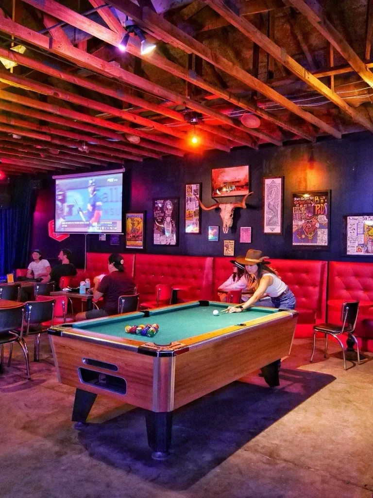 Woman playing pool in a dimly lit bar with eclectic decor.