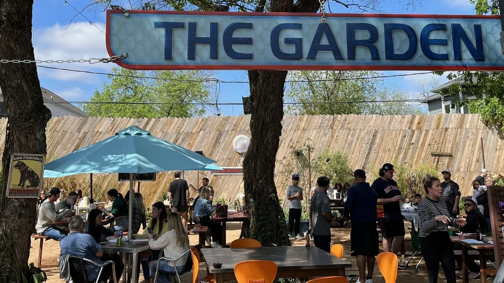 Outdoor beer garden, patrons at tables, "THE GARDEN" sign.