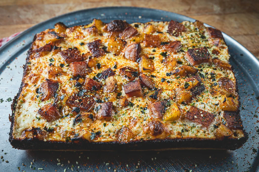 Detroit-style deep-dish pizza with meat, potatoes, and various seasonings.