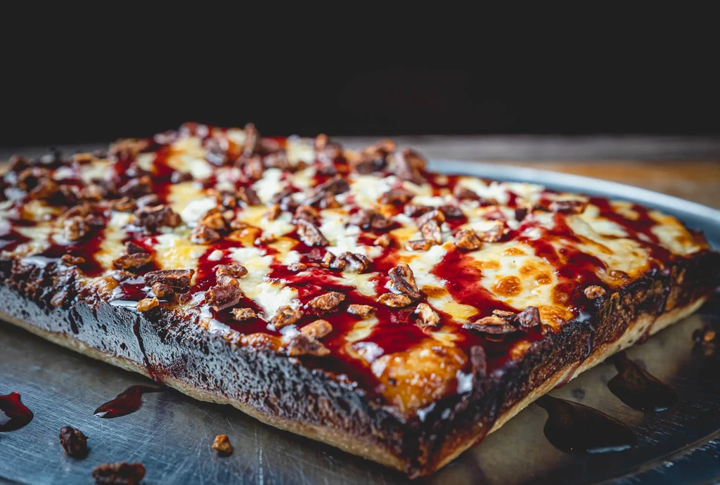 Deep-dish pizza or flatbread with cheese, red sauce, and nuts.
