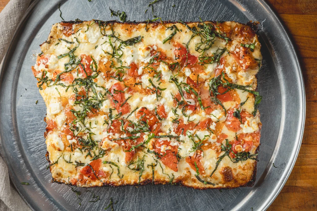 Rectangular pizza with melted cheese, diced tomatoes, and basil.