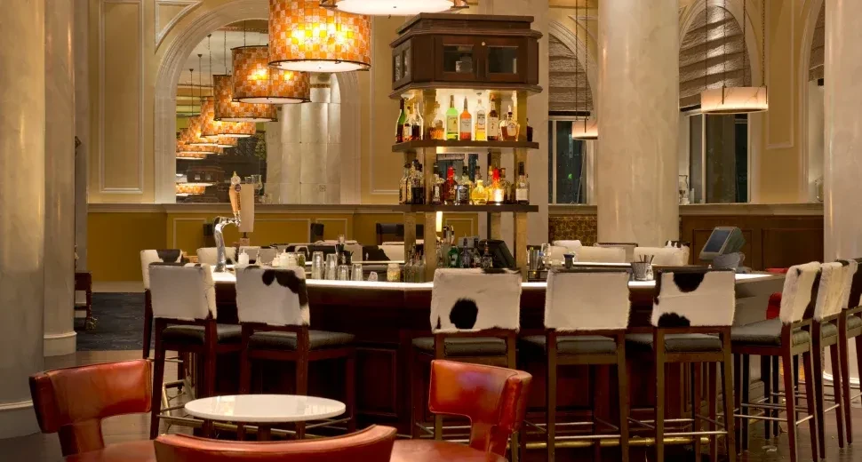 Sophisticated bar area with cowhide stools and illuminated liquor bottles.