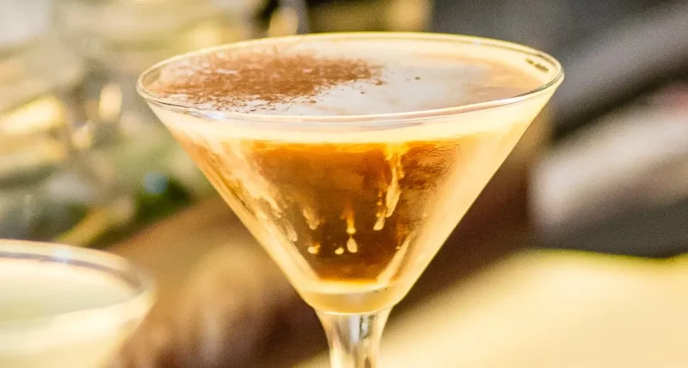 Martini glass with layered brown and amber beverages, dusted powder.