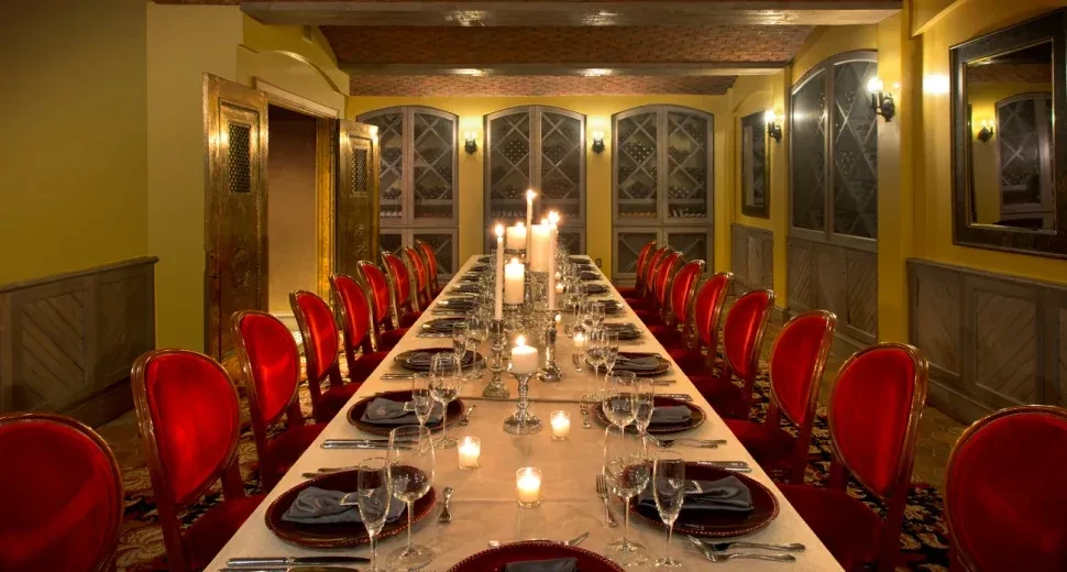 Luxurious private dining room with long candlelit table and red velvet chairs.