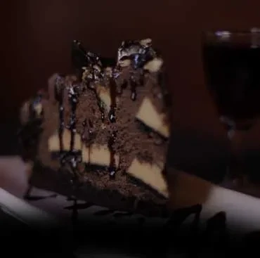 Chocolate cake slice with chocolate sauce and cookie pieces.