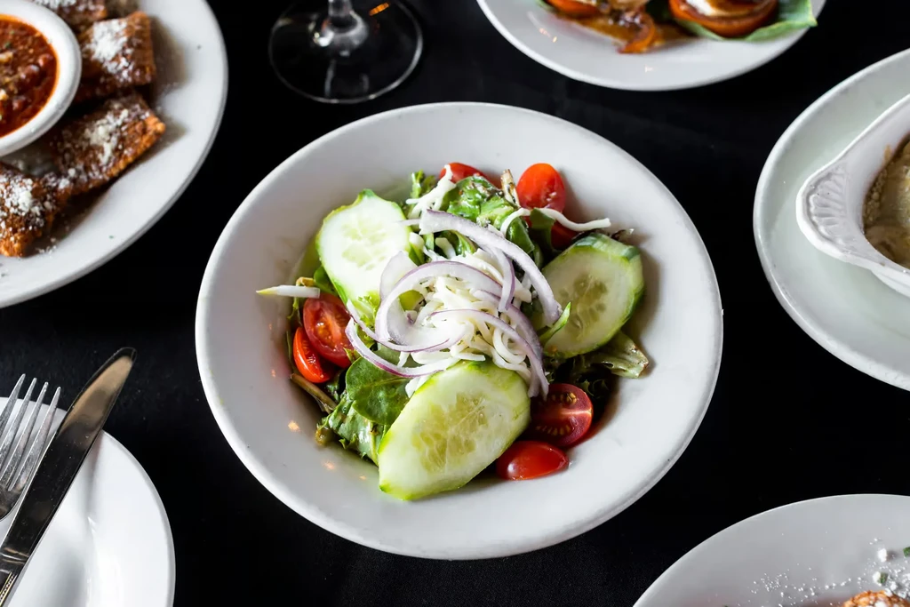 Overhead view of a salad bowl and appetizers on a dark table.