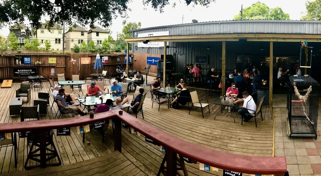 Outdoor wooden patio with people and a Karbach Brewing Co. sign.