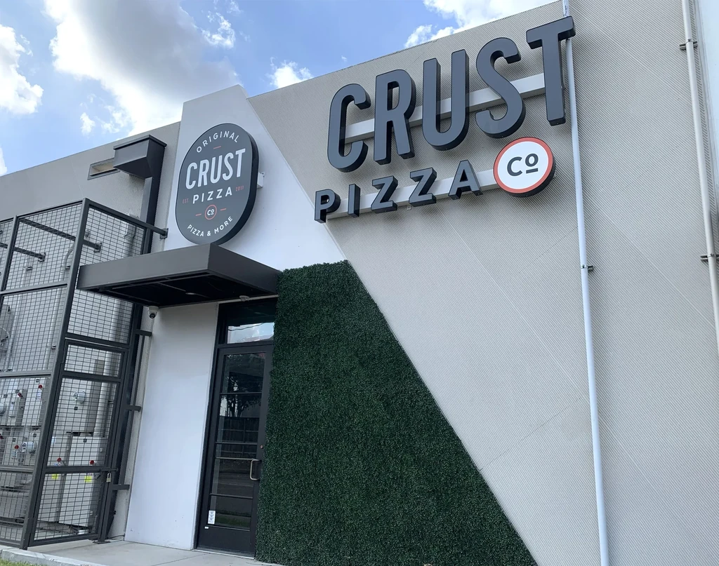 Exterior of Crust Pizza Co. restaurant with artificial turf wall.