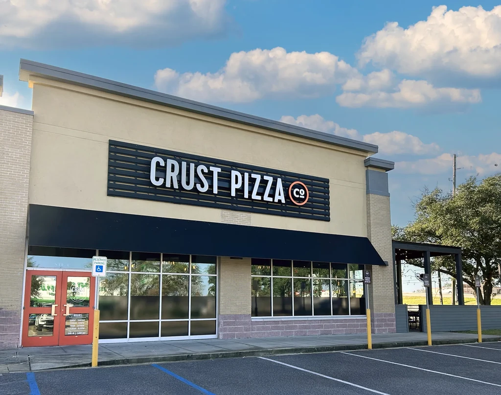 Exterior of Crust Pizza Co. restaurant with patio and parking lot.