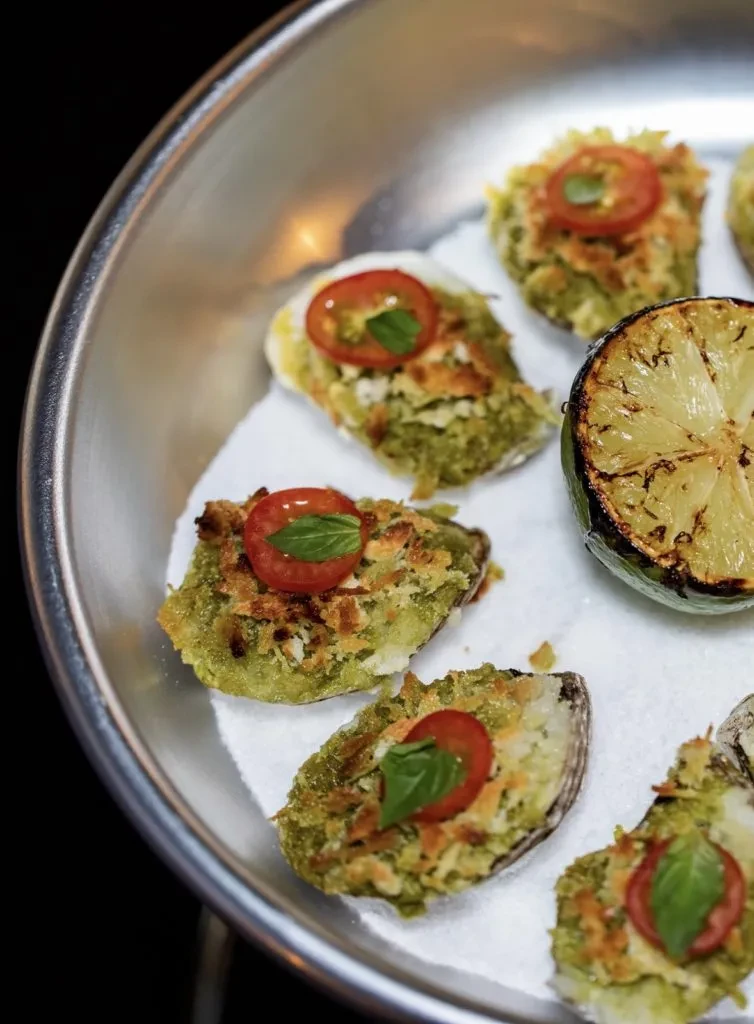Baked oysters topped with cherry tomato, basil, and a grilled lime.