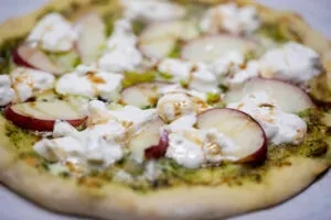 Close-up of a pesto pizza topped with apple and cheese.