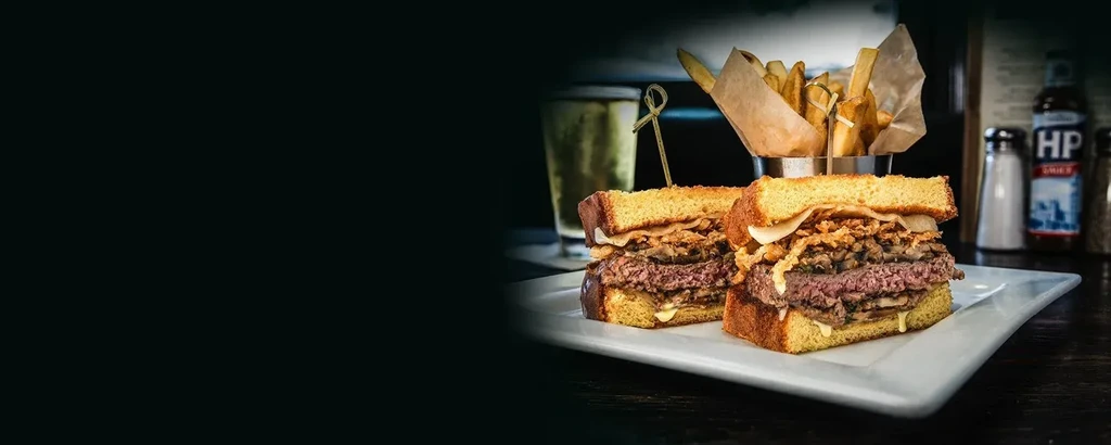 Stacked burger with cheese, mushrooms, and fries on a white plate.