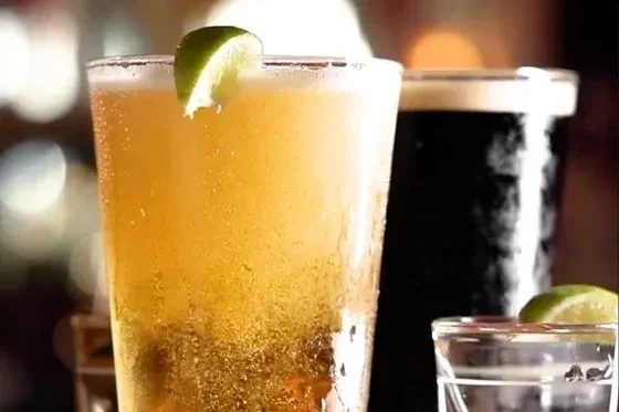 Three glasses of beer and a shot glass, two with lime.