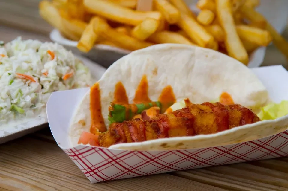 Close-up of a fried taco, coleslaw, and fries on a wooden table.
