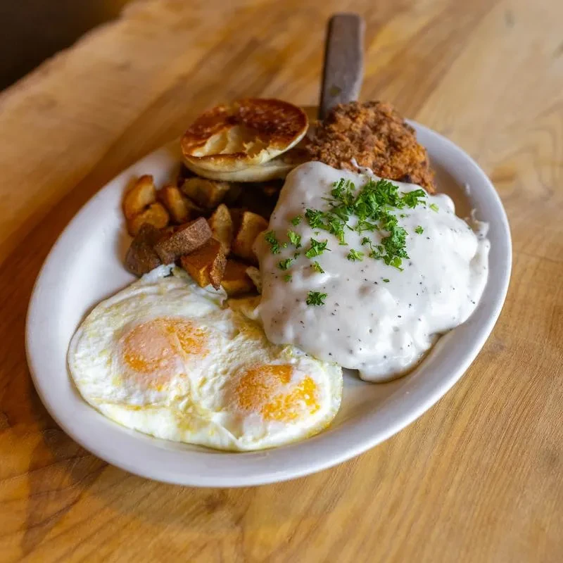 Breakfast platter: two sunny-side-up eggs, gravy-smothered steak, potatoes, biscuit.