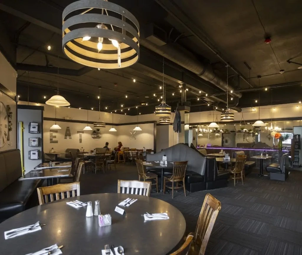 Industrial-chic restaurant interior with 'EAT' sign, varied seating, and warm lighting.