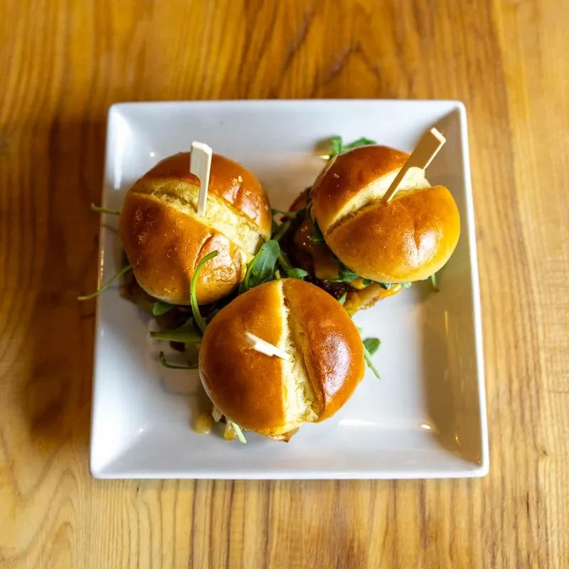Three sliders with golden buns, greens, and skewers on a white plate.