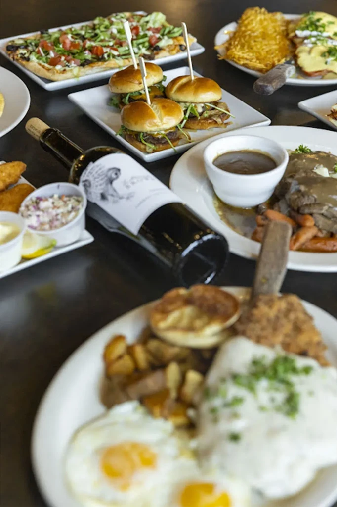 A diverse food spread featuring flatbread, mini-burgers, pot roast, and wine.
