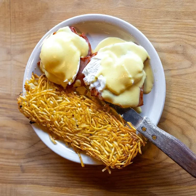 Close-up plate of Eggs Benedict, hollandaise sauce, and crispy hash browns.