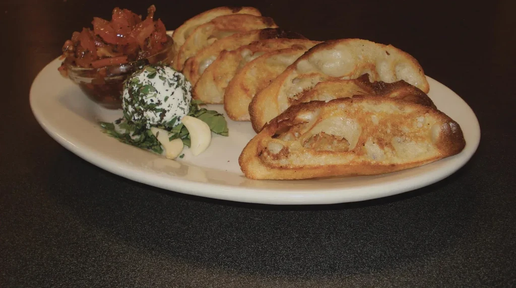 Close-up of crostini, orange relish, herb cheese ball, and garlic.