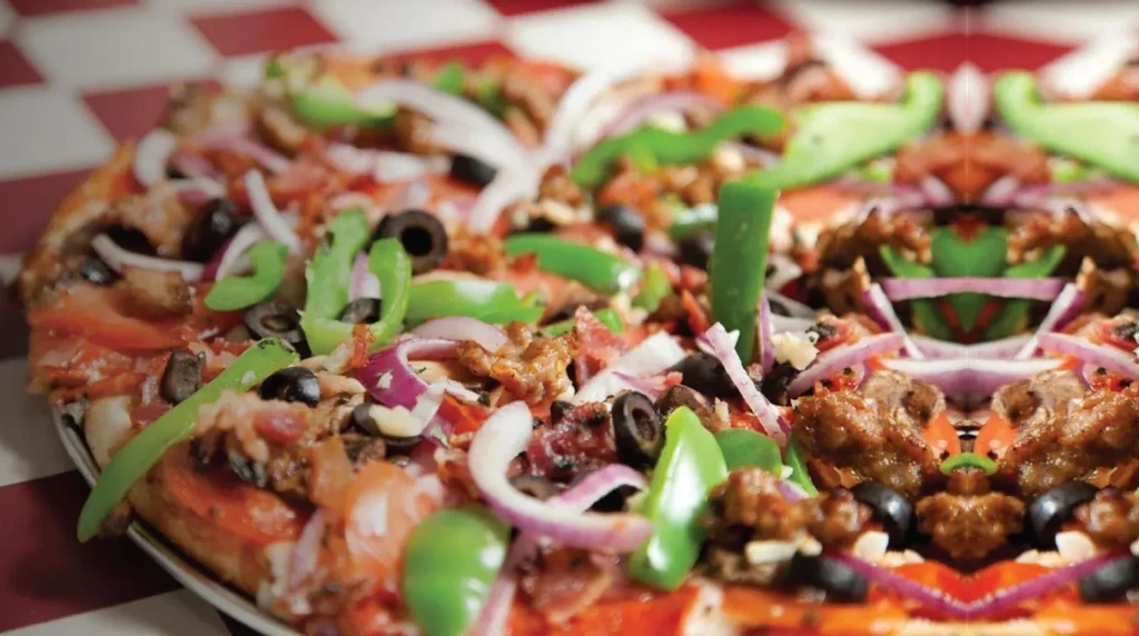 Topped pizza with vegetables, meat, and a prominent mirrored effect.