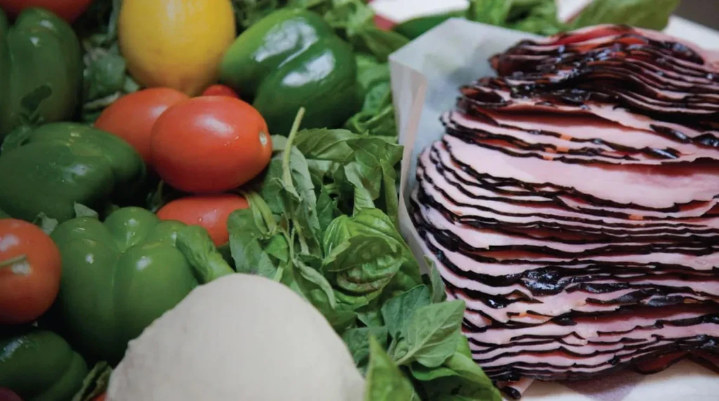 Close-up of fresh peppers, tomatoes, herbs, sliced meat, and mozzarella.