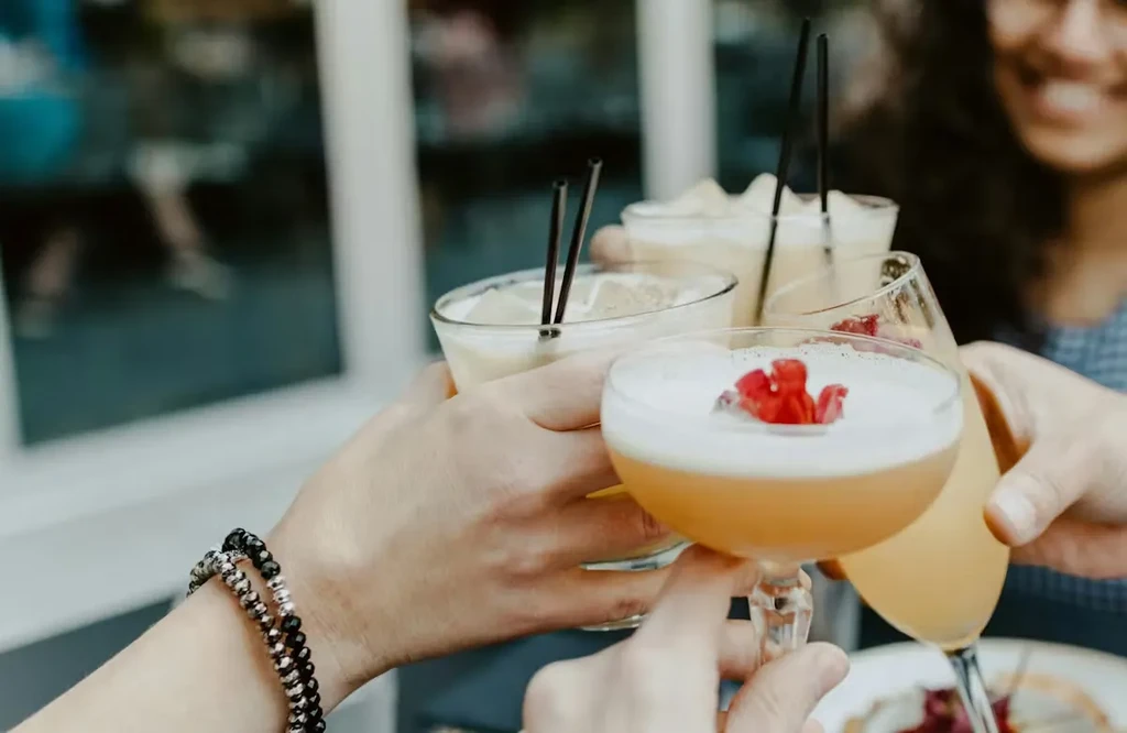 Multiple hands clinking four different cocktail glasses in a toast.