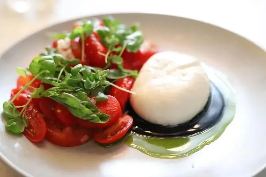 Plated burrata, cherry tomatoes, and basil with balsamic and olive oil.