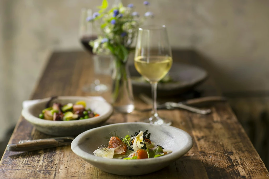 Beautifully set rustic restaurant table with two dishes, wine, and flowers.