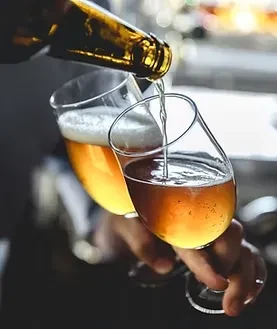 Hands pour golden amber beer into two stemmed glasses.