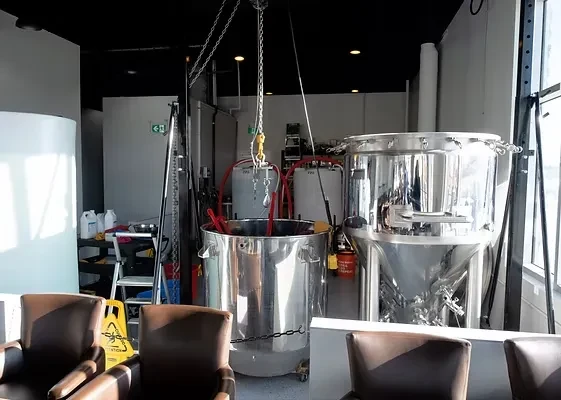 Industrial microbrewery with shiny tanks, red hoses, and seating area.