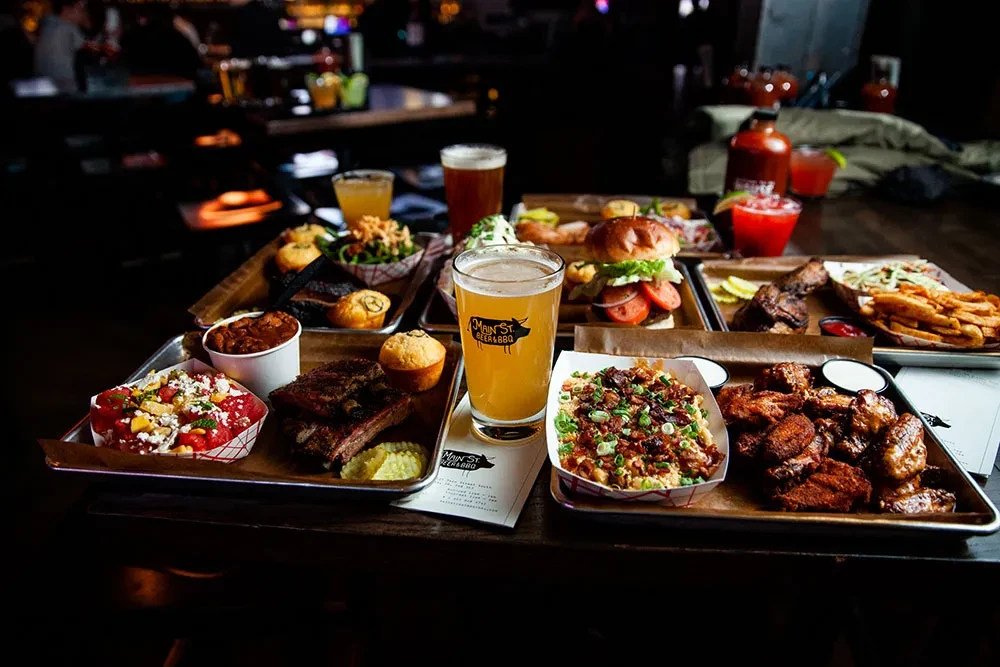 Restaurant table laden with burgers, ribs, wings, mac and cheese, and cocktails.