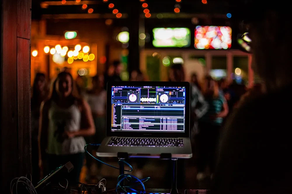 DJ laptop with mixing software, blurred club lights and crowd.