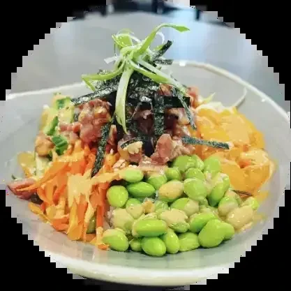 Close-up poke bowl: raw fish, edamame, carrots, green onions, and seaweed.