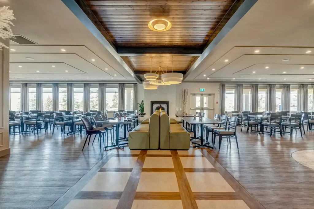 Symmetrical, unoccupied elegant dining hall with seating, fireplace, and large windows.