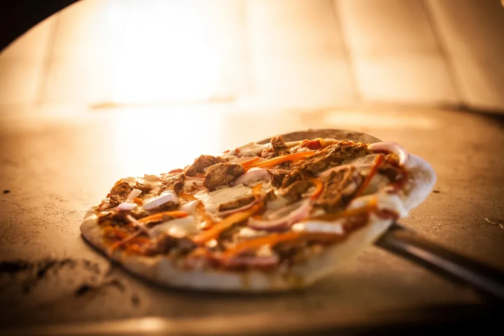 Partially cooked pizza on a peel entering a glowing oven.