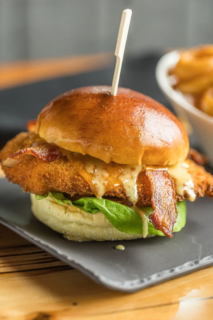 Crispy fried chicken sandwich with bacon, cheese, and lettuce on a plate.