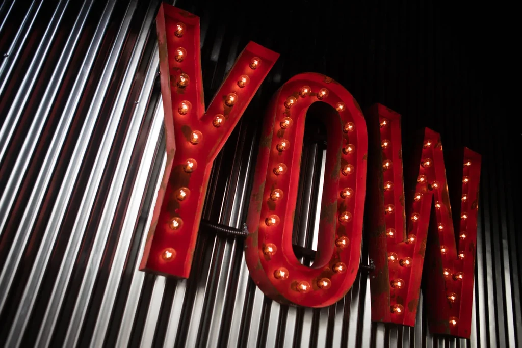 Rustic red 'YOW' sign with incandescent bulbs on corrugated metal.