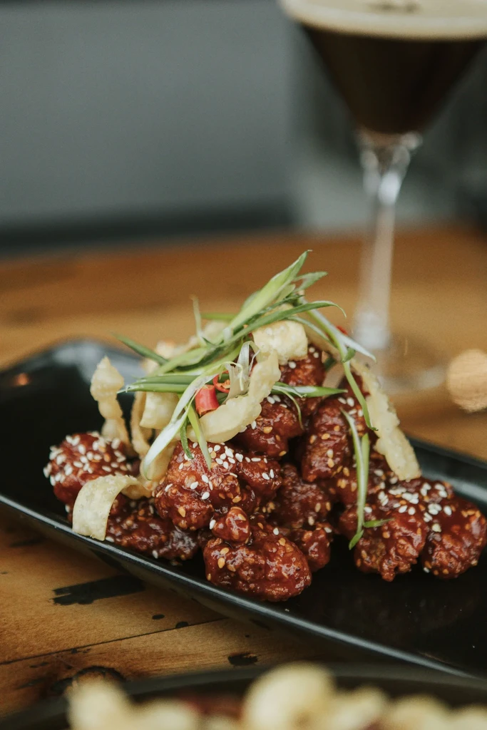 Mound of glazed chicken bites with sesame, green onions, chili, crispy strips.
